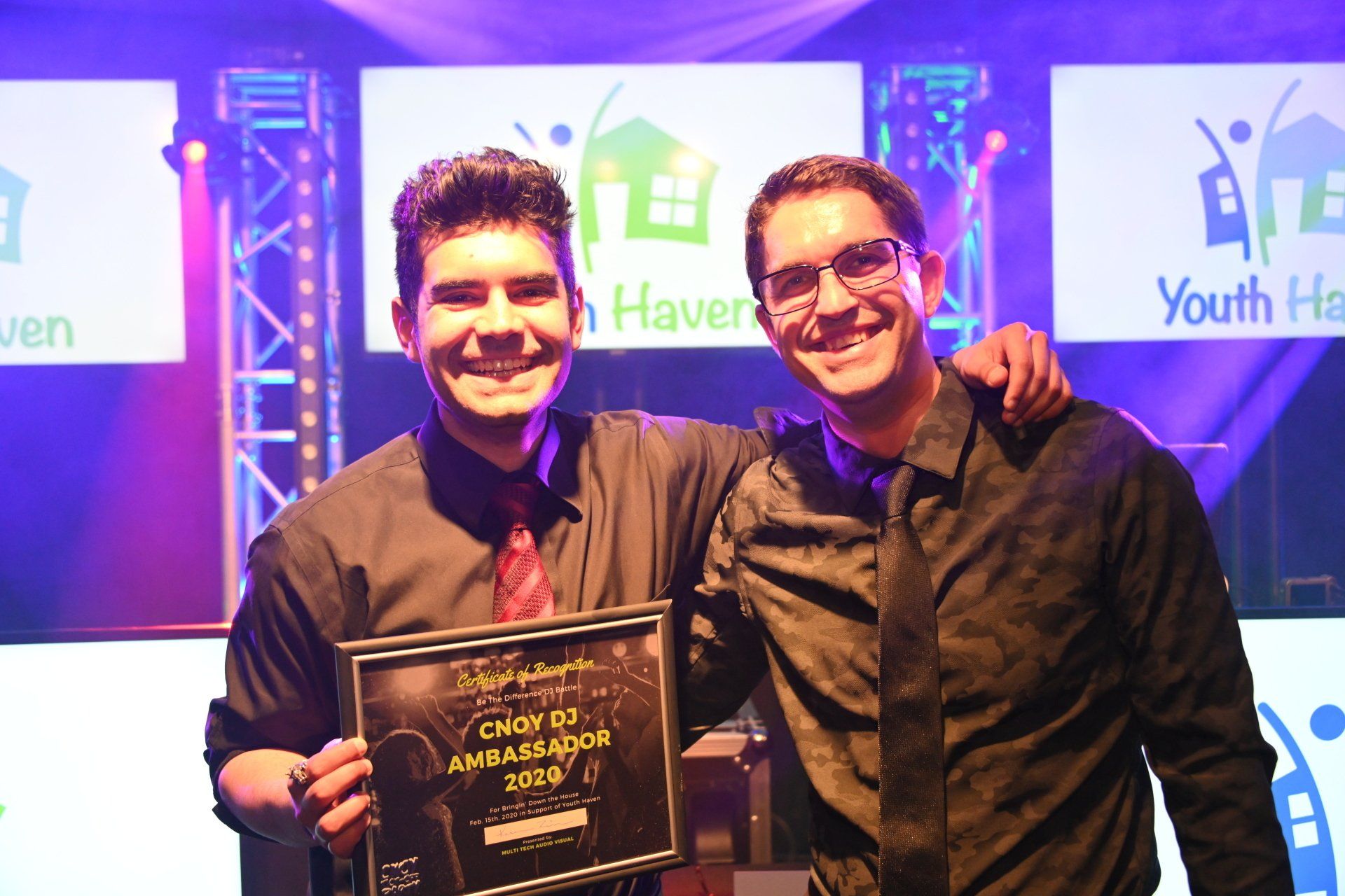 Two men smiling, holding an award on a stage with 