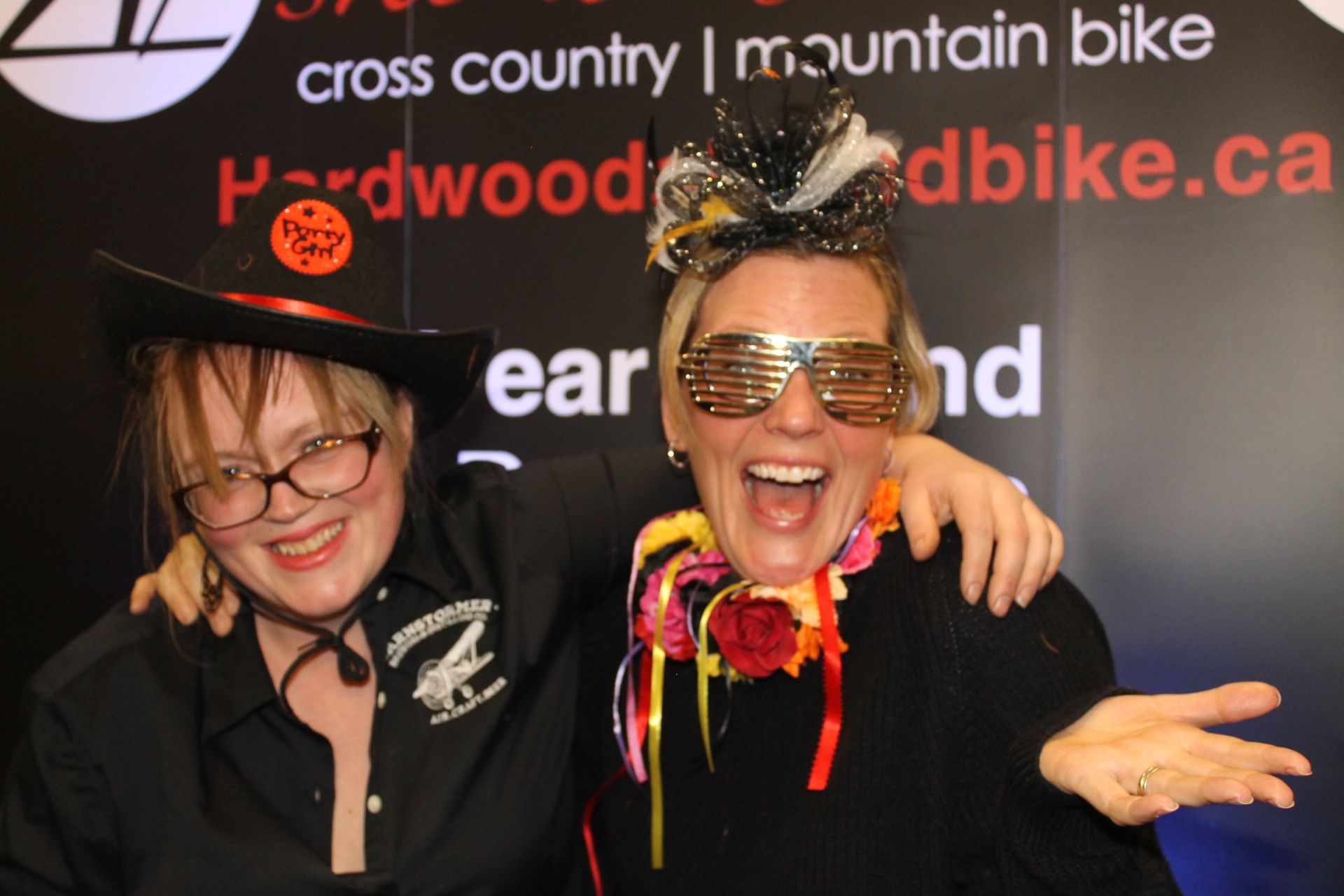 Two smiling people pose, one in a witch hat and glasses, the other in novelty sunglasses and a garland.