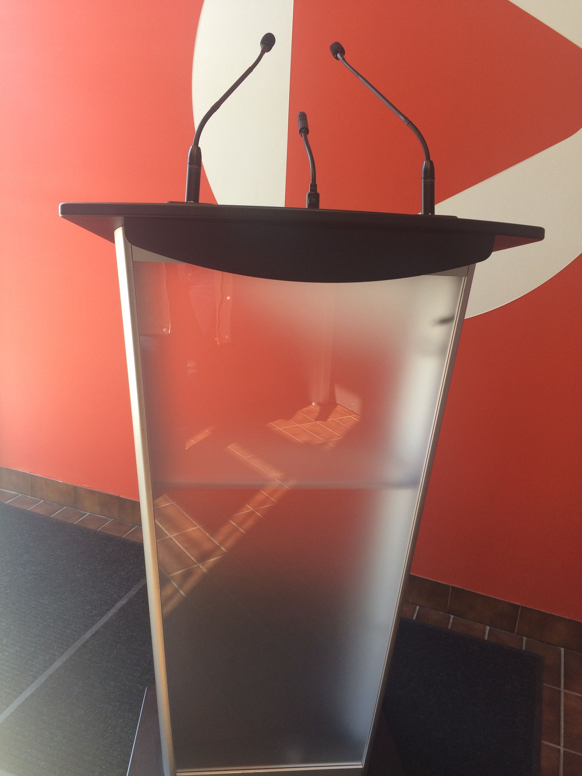 Podium with microphones in front of a red and white background.