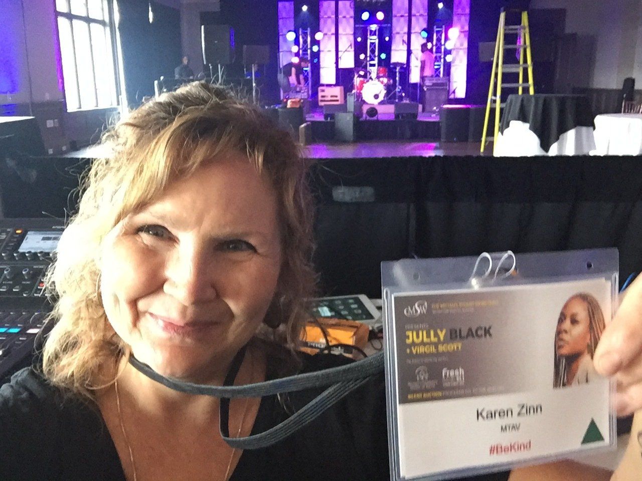Woman smiling, holding a backstage pass labeled 