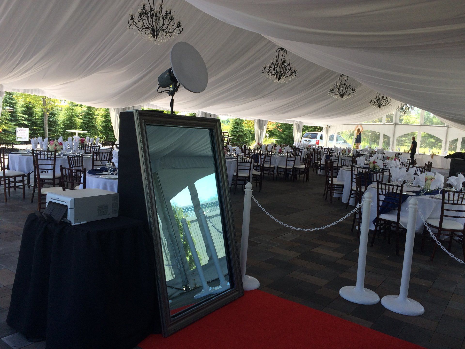 Photo booth setup at an outdoor event: mirror, projector, red carpet, and tables under a tent.