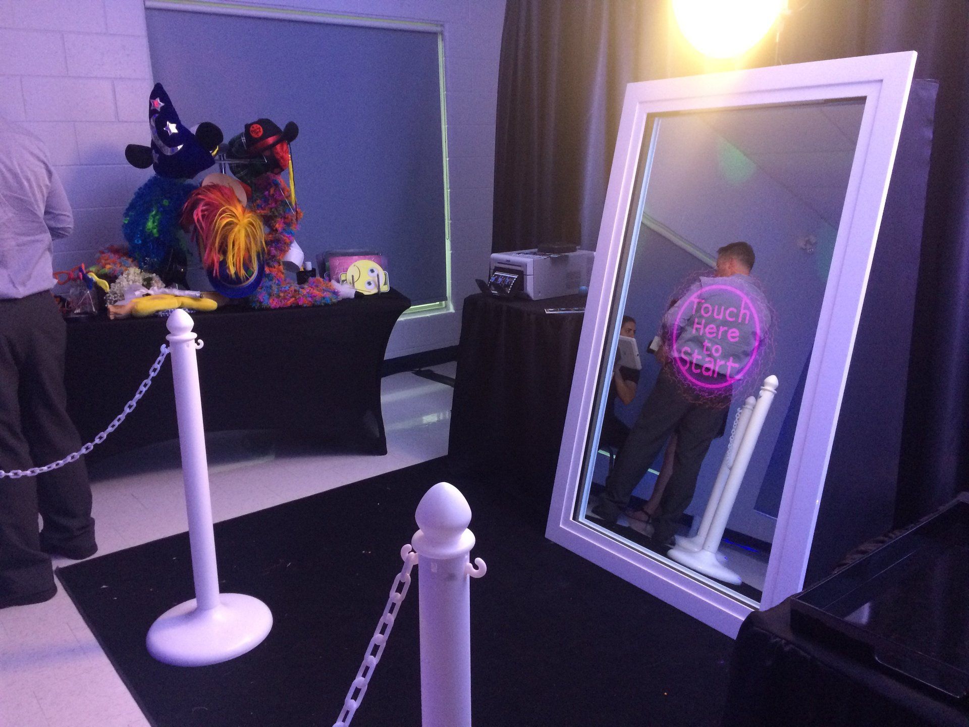 Photo booth with a mirror, props on a table, and a person taking a photo.
