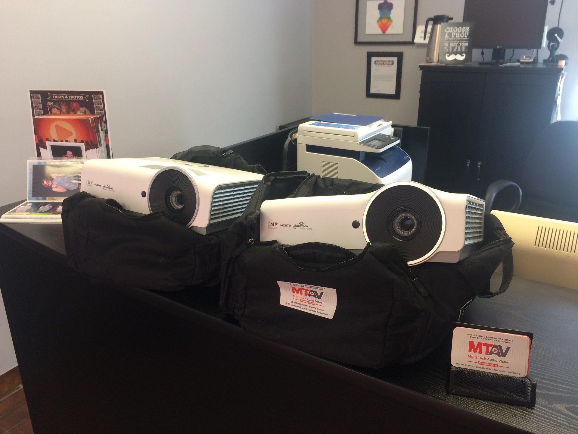 Two white projectors in black carrying cases on a desk, next to a printer and business card holder.