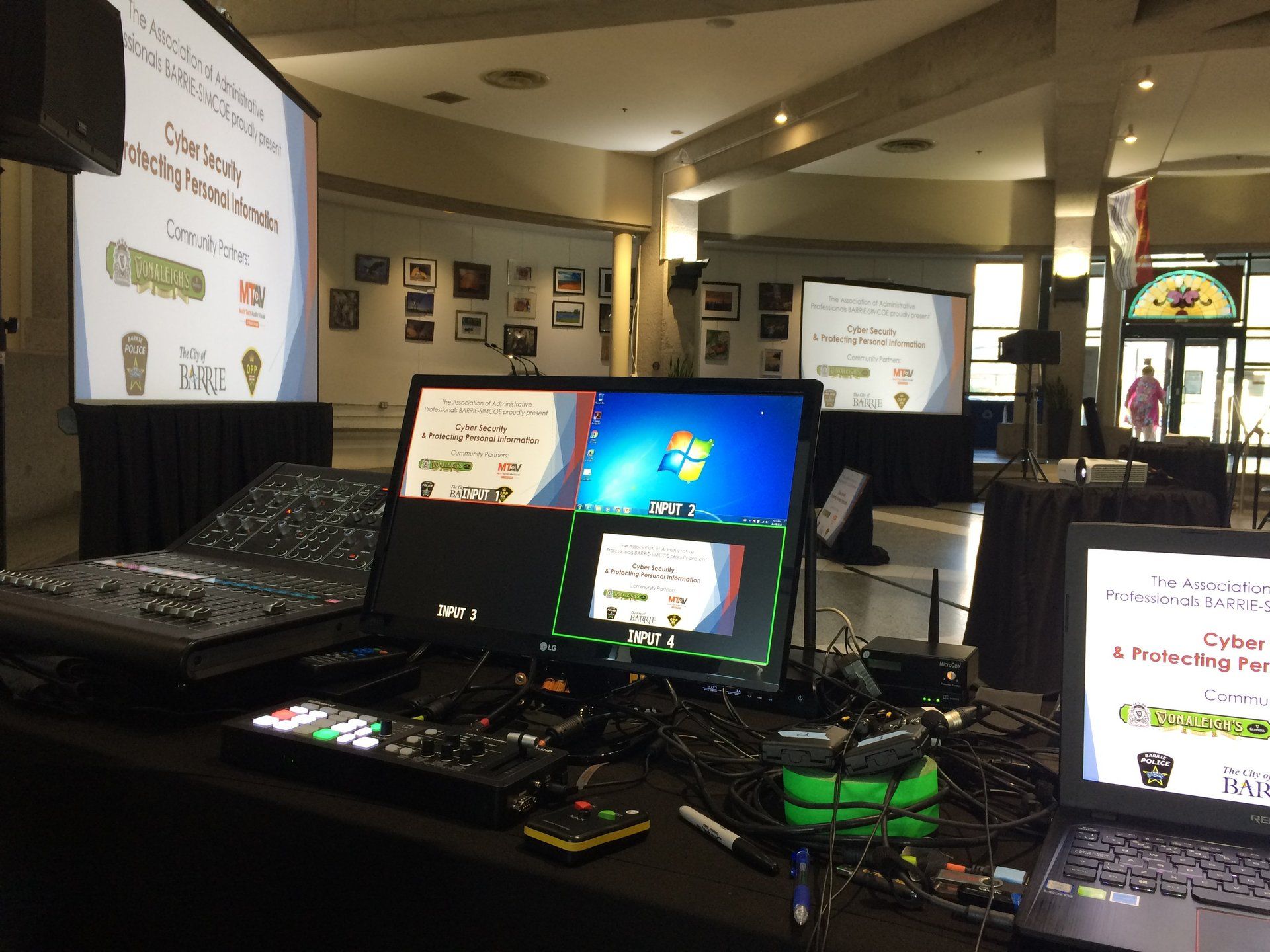 Event setup: Screens, mixing board, laptops, cables in a conference hall with presentations on screens.