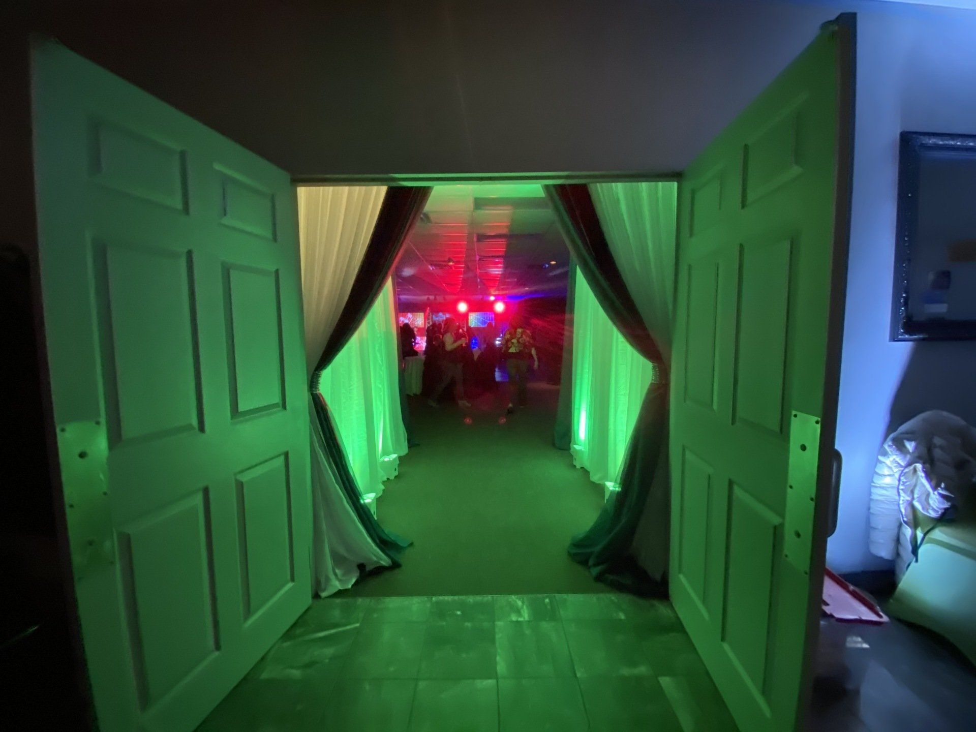 Open double doors lead to a lit hallway with a green floor. People and red/blue lights visible at the end.