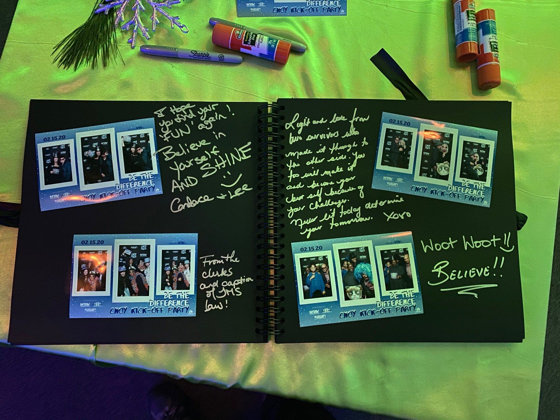 Black scrapbook with instant photos and handwritten messages. Glue sticks, pens, and lavender sprig are nearby.