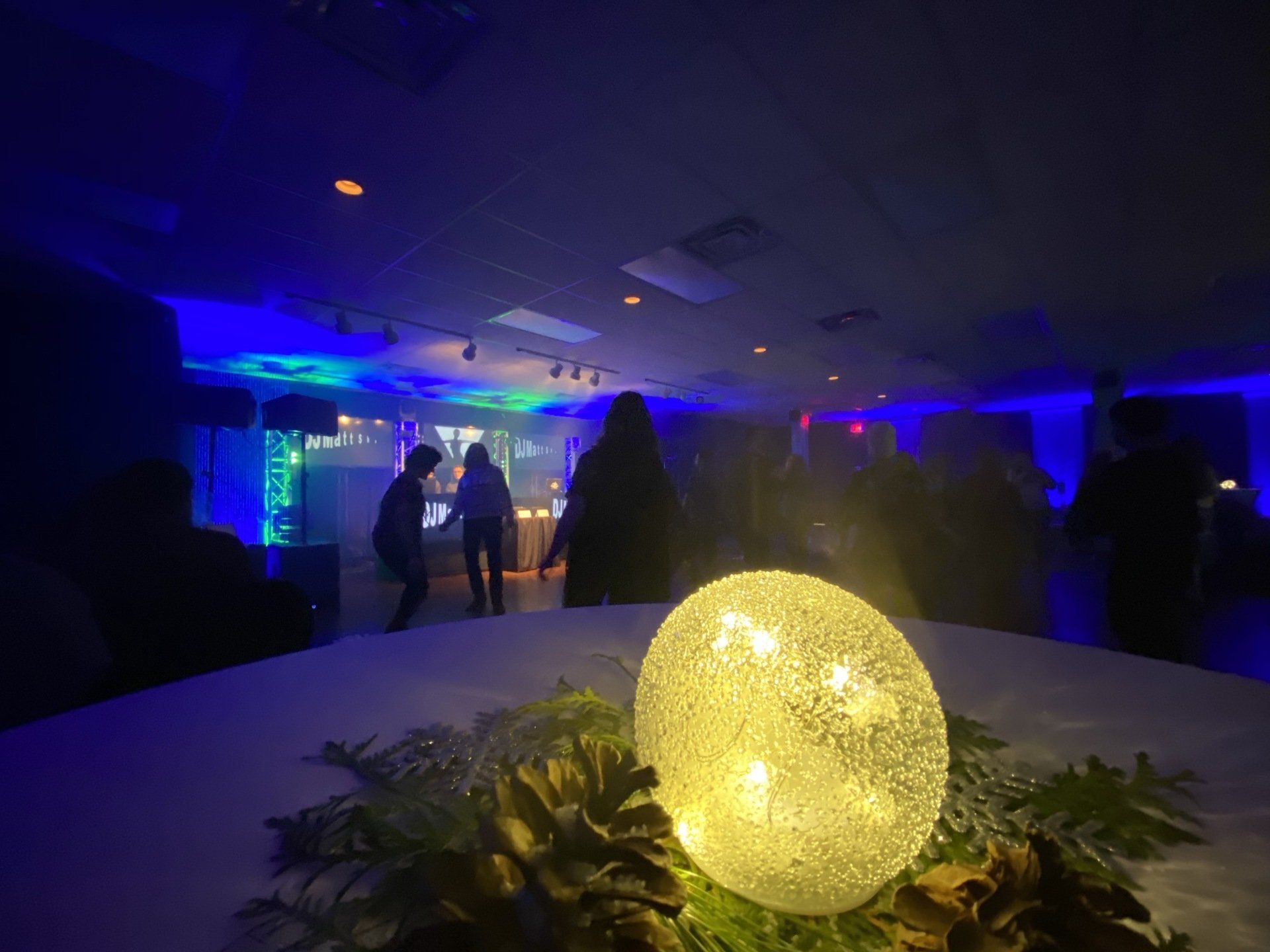 A lit, glowing sphere on a table in front of a blue-lit room with people dancing.