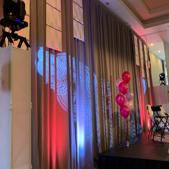 Stage with gray curtains, lit with red and blue lights, balloons, and event lights.
