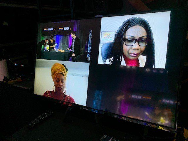 A screen displaying a virtual meeting: two women, and two people near a table with lighting.