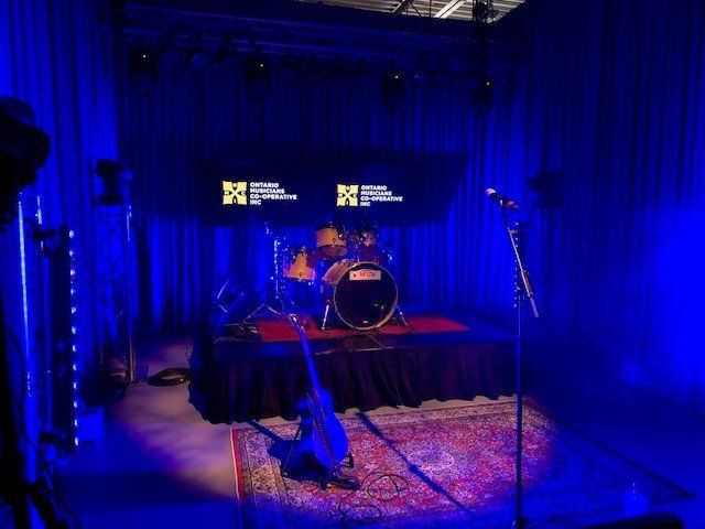 Stage with drums, microphone, and guitar under blue lights, banners displayed.