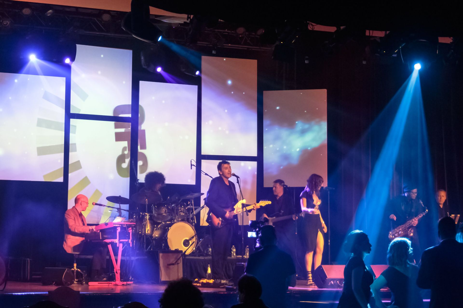 Band performing on stage with colorful lights and background screens.