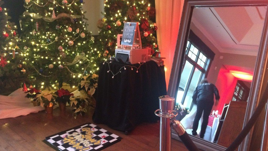 Christmas tree and mirror photo booth set up for an event, person visible in reflection.