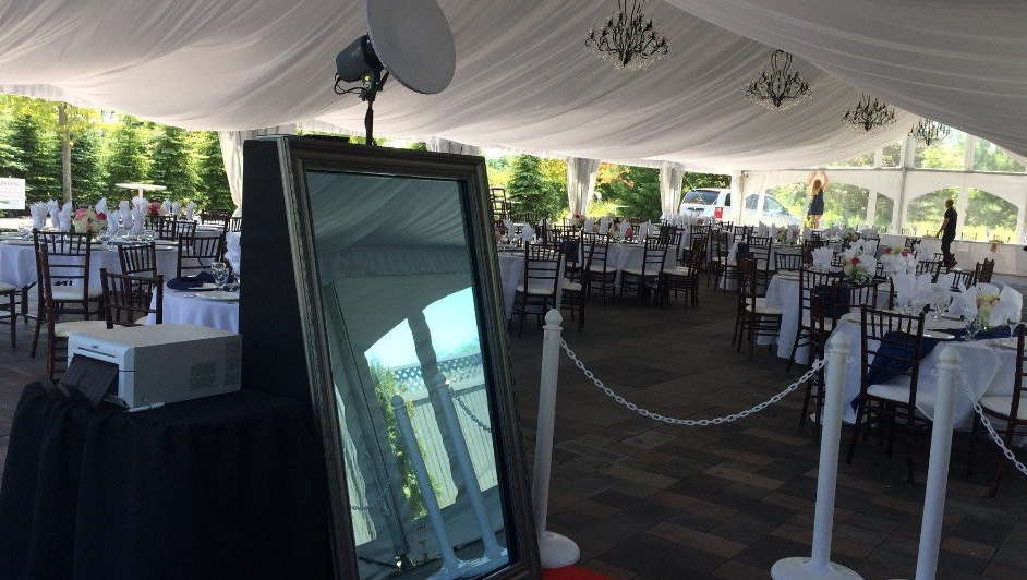 A photo booth with a mirror and a printer set up in a tented wedding reception.