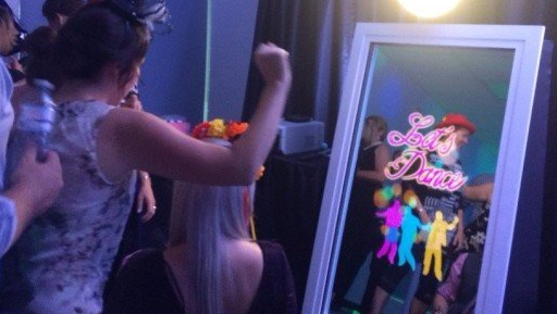 People at a party pose for a photo with props in front of a mirror.