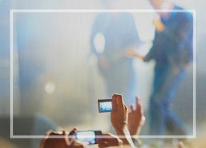 Person recording a concert with a phone. Stage and performers are blurred in background.