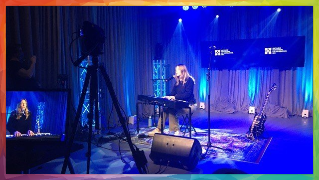 Woman performing music on stage, playing keyboard and singing with blue stage lighting.