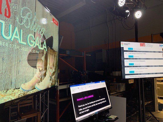 Event setup with screens displaying information:  promotional image, text, and operational content.  Black equipment and lighting are visible.