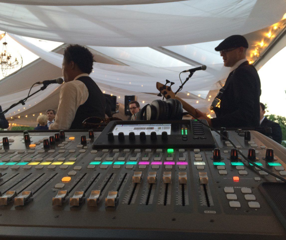 Soundboard with two musicians performing at an outdoor event under a white canopy.