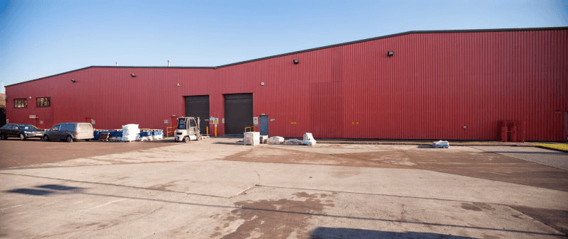 Red industrial warehouse with loading dock doors and a paved lot under a clear sky