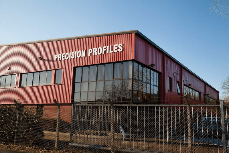 Precision Profiles industrial building with red siding and fenced perimeter under a clear sky