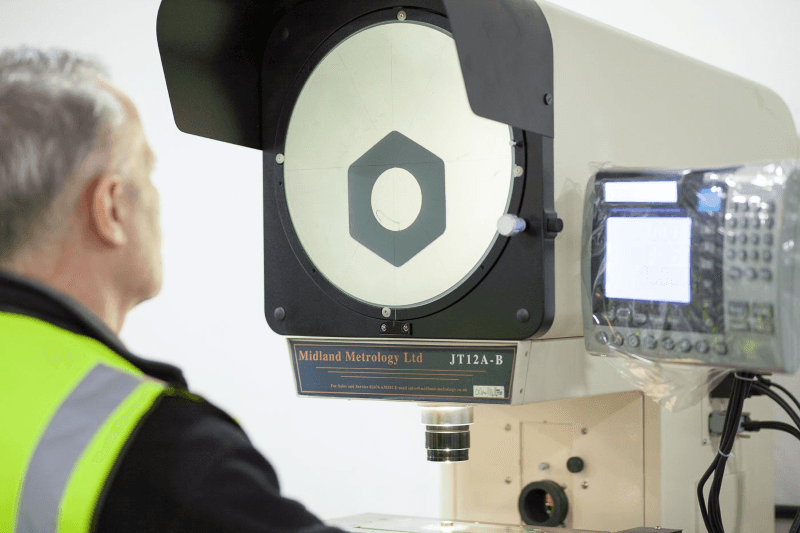 Technician in a safety vest using a CMM machine with a display screen in an industrial setting