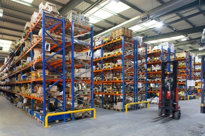 Large warehouse with tall orange-and-blue storage racks and a forklift on a concrete floor.