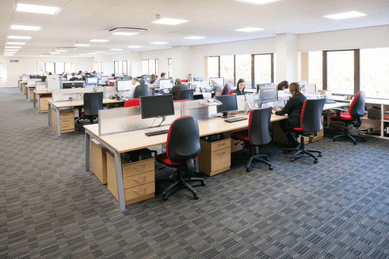 Open-plan office with desks, computers, and people working at cubicles