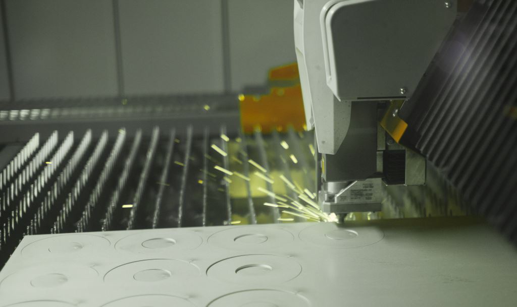 Industrial machine cutting sheet metal with sparks flying inside a workshop