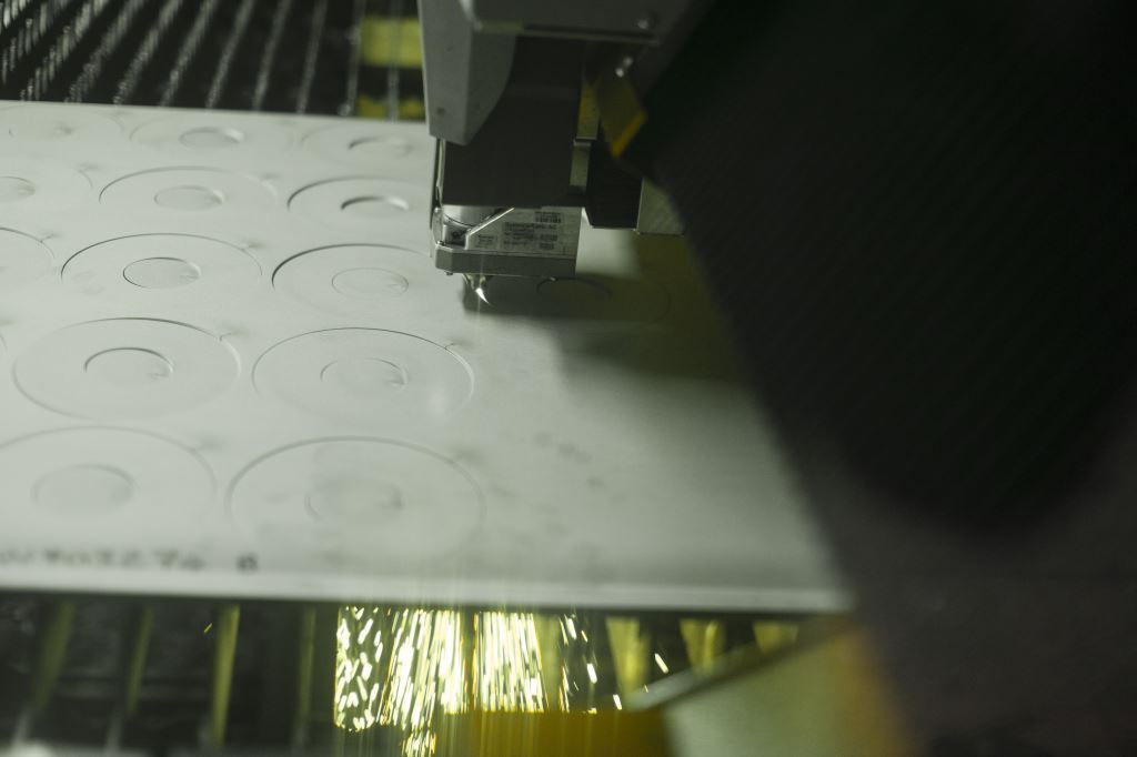Industrial machine cutting circular patterns in a light-colored sheet of metal