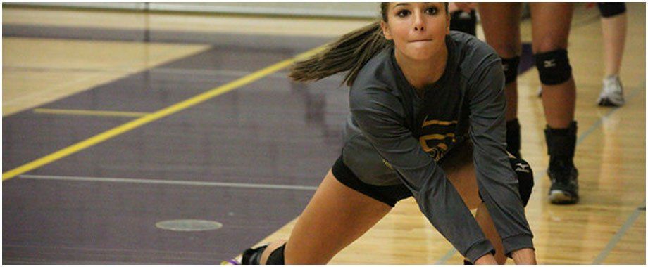 A female volleyball player is kneeling down on the court