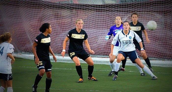 A group of female soccer players are playing a game on a field.