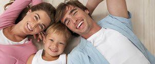 A family is laying on the floor together and smiling.