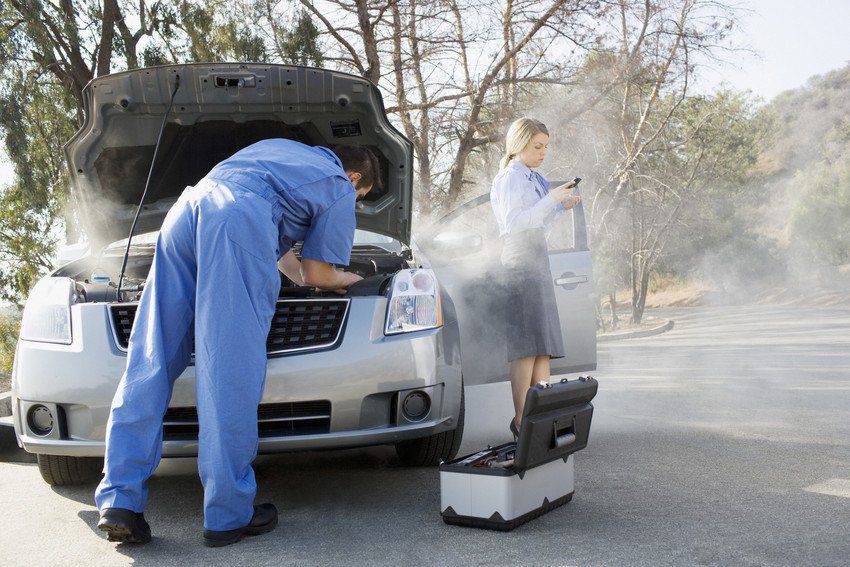 Businesswoman using cell phone while mechanic looks at car engine