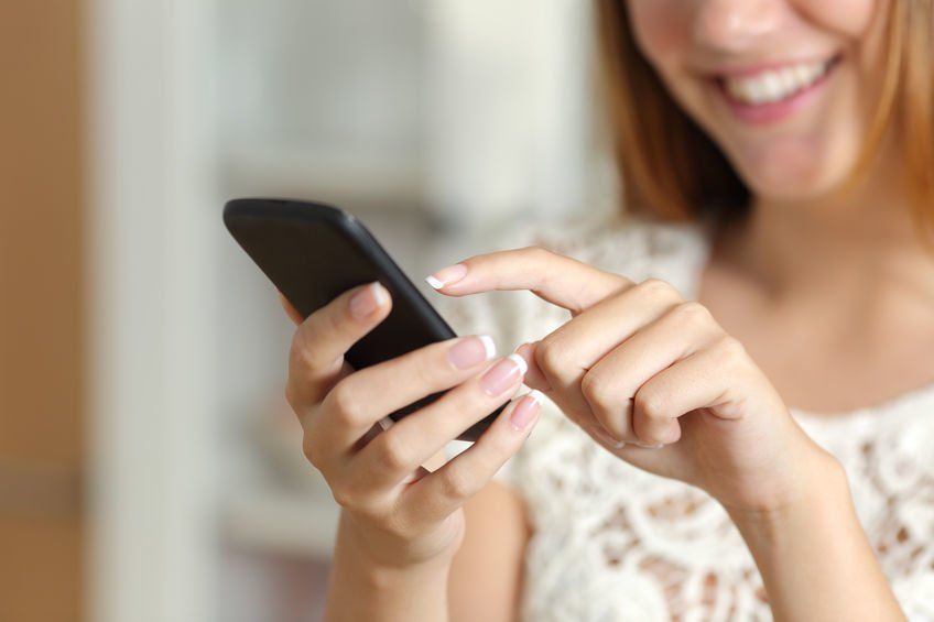 A woman is smiling while using her cell phone.