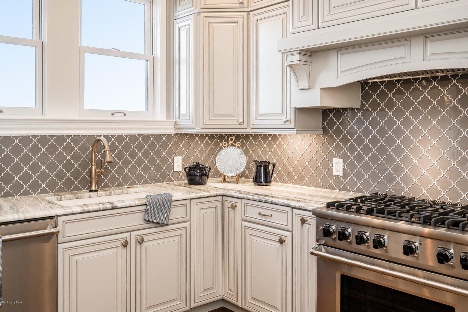 Cream-colored kitchen with gray tile backsplash, stainless steel appliances, and a window.