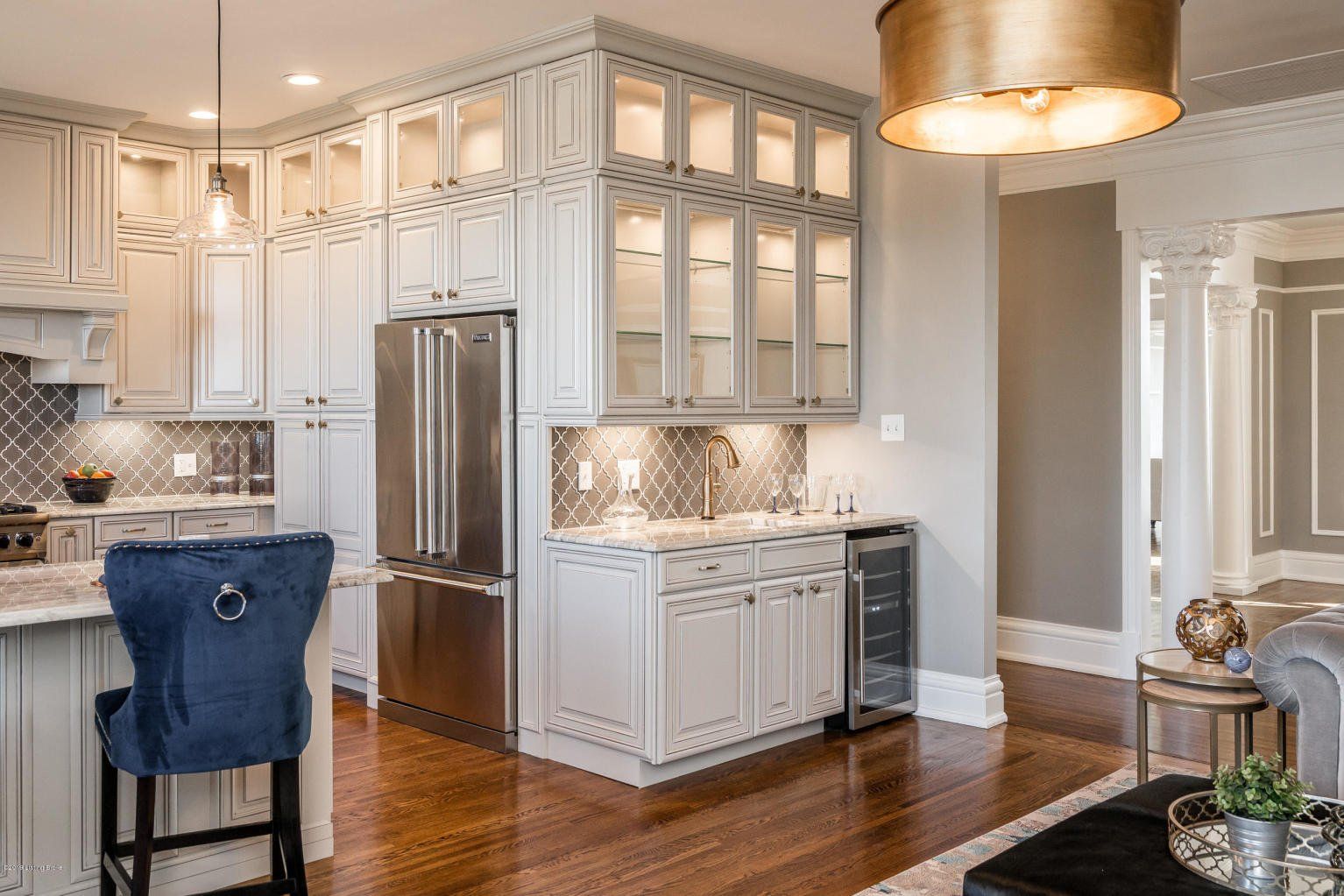 Gray kitchen with cabinets, stainless steel refrigerator, blue bar stool, and wooden floor.