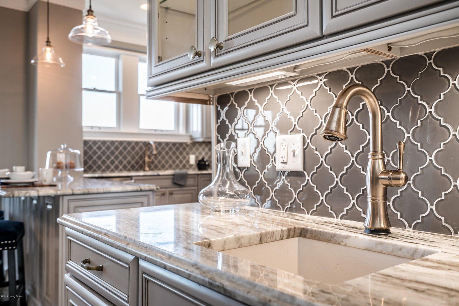 Kitchen with gray cabinets, marble countertops, patterned backsplash, and gold faucet.