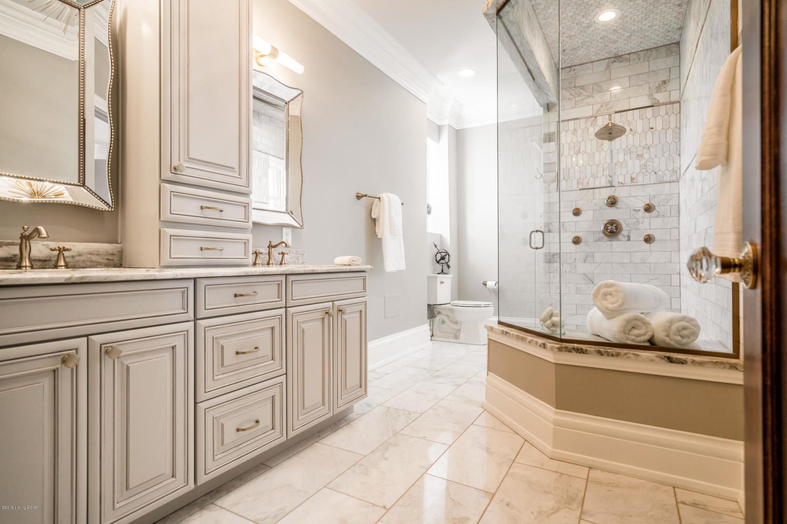 Spacious light gray and white bathroom with marble floors, a glass shower, and vanity.