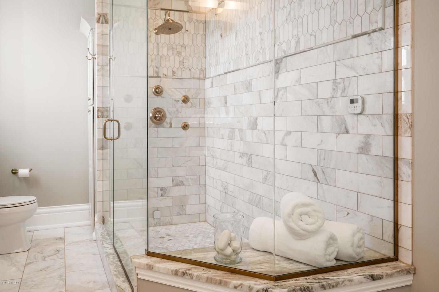 Luxurious bathroom with marble tile and glass shower enclosure; towels on a ledge.