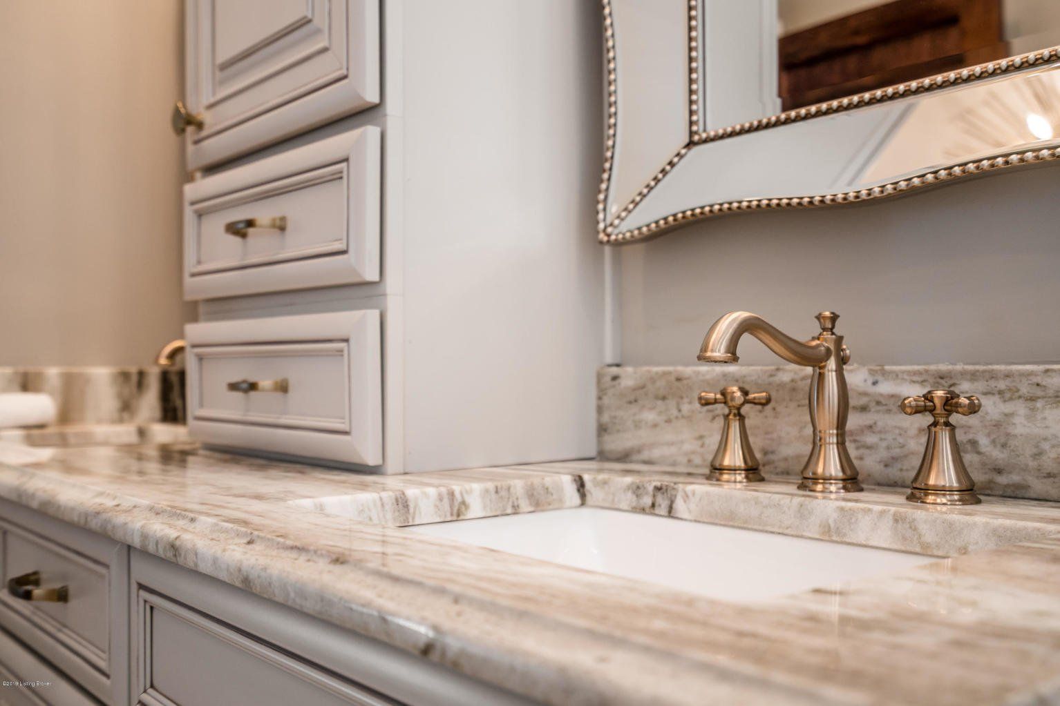 Elegant bathroom vanity with marble countertop, brass faucet, and decorative mirror.
