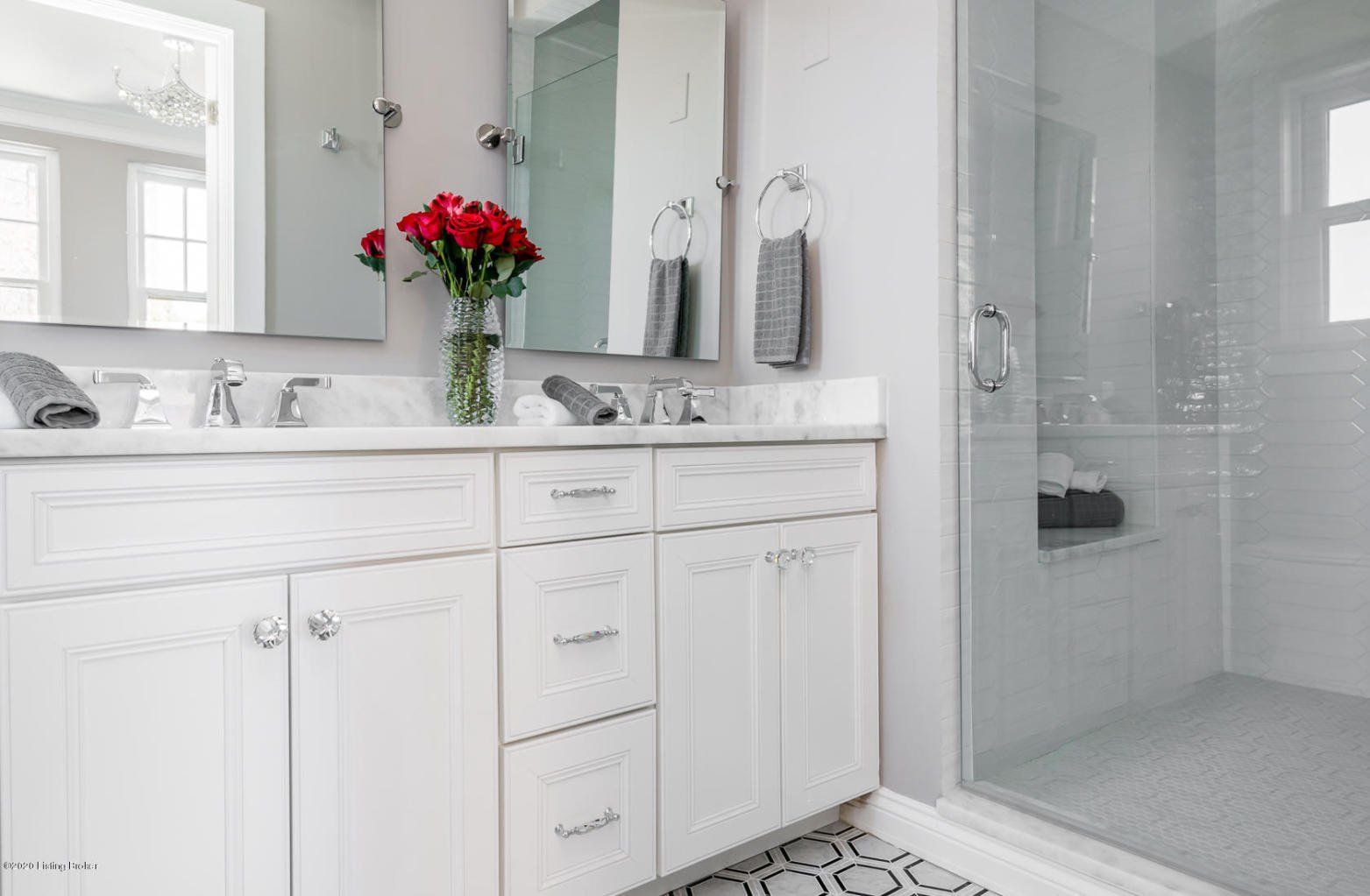 White bathroom with double vanity, large mirrors, shower, and red roses.