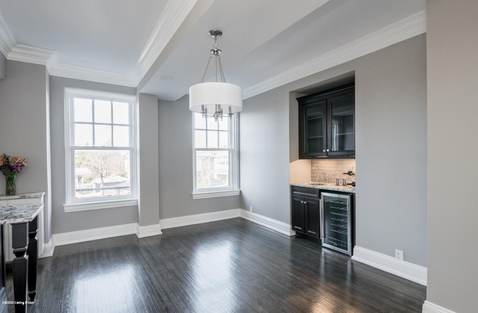 Empty dining room with dark wood floor, grey walls, and built-in black bar area.