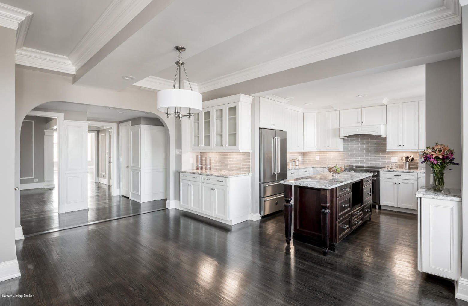Spacious white kitchen with dark wood floors, island, stainless steel appliances, and arched doorway.