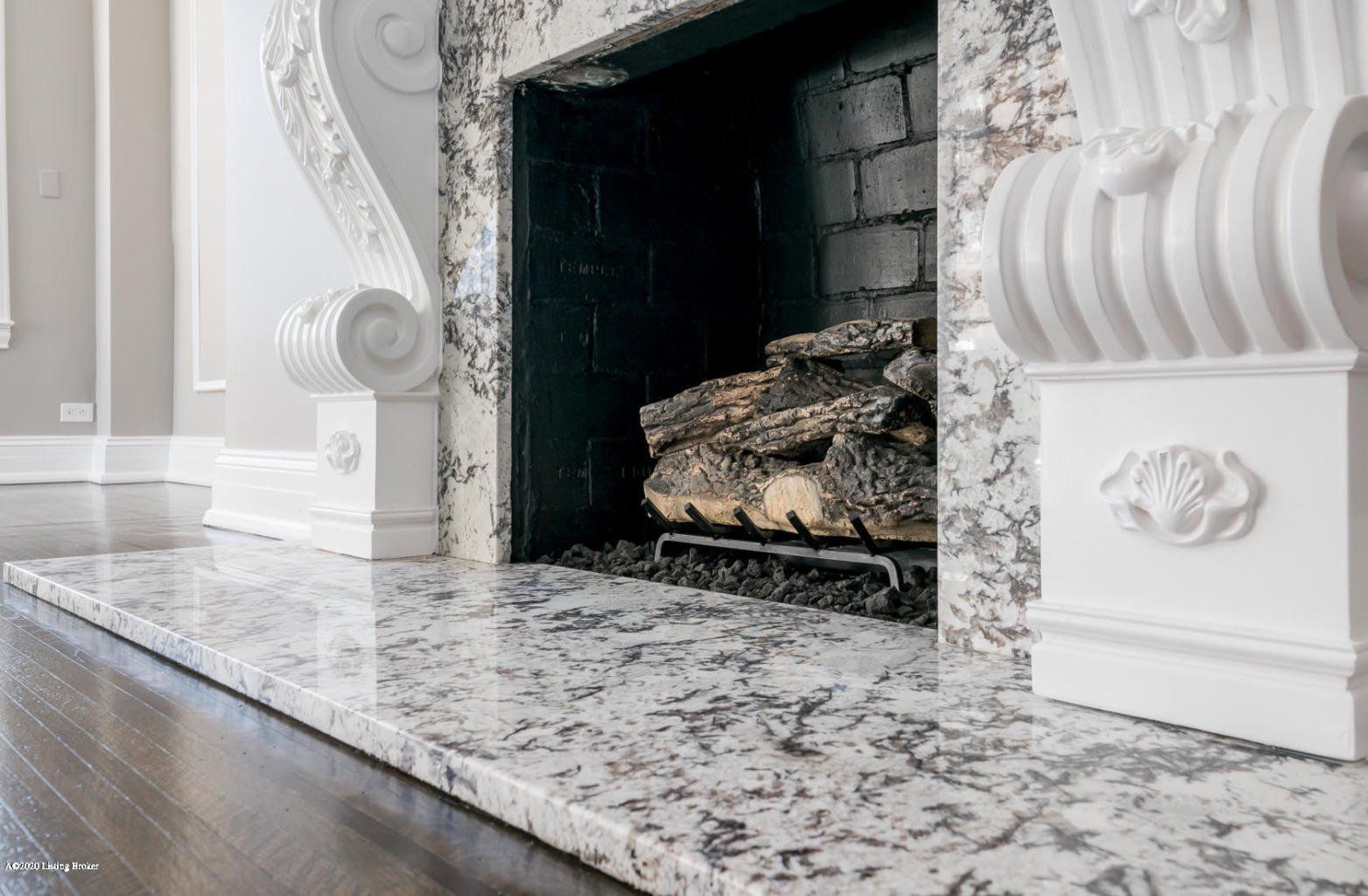 Fireplace with granite surround and white decorative accents. Dark wood floor.