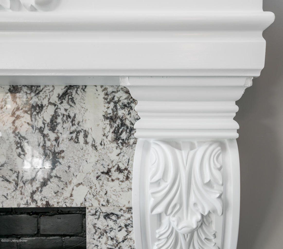 White ornate fireplace mantel with granite background.