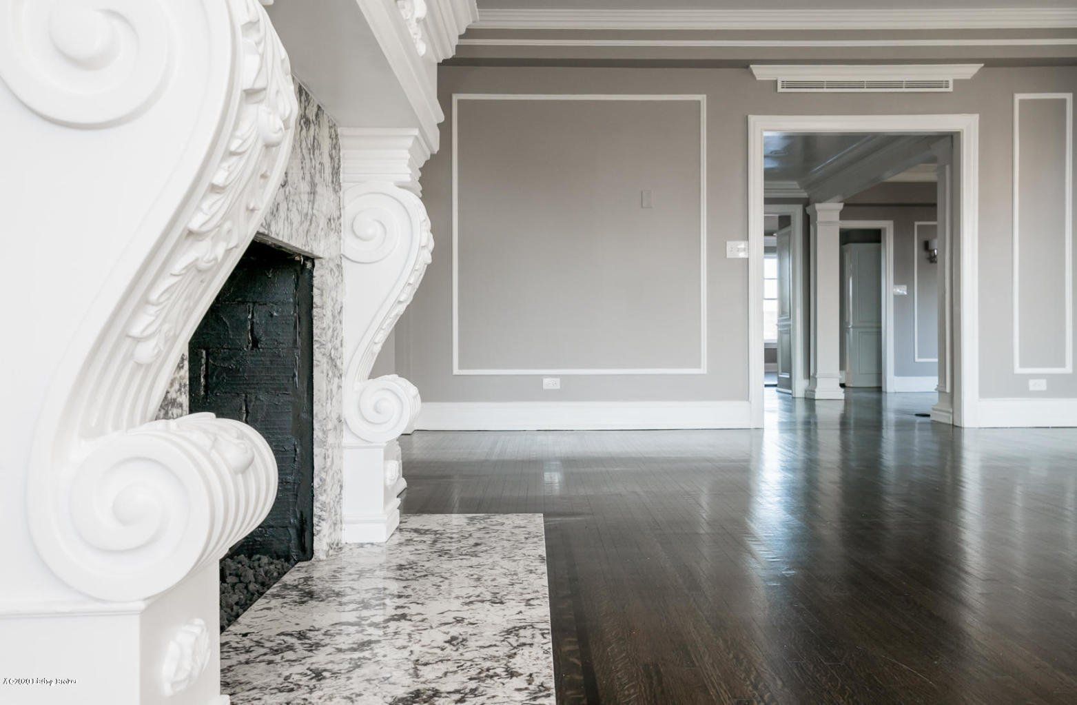 Ornate white fireplace in an empty room with gray walls and dark wood floors.