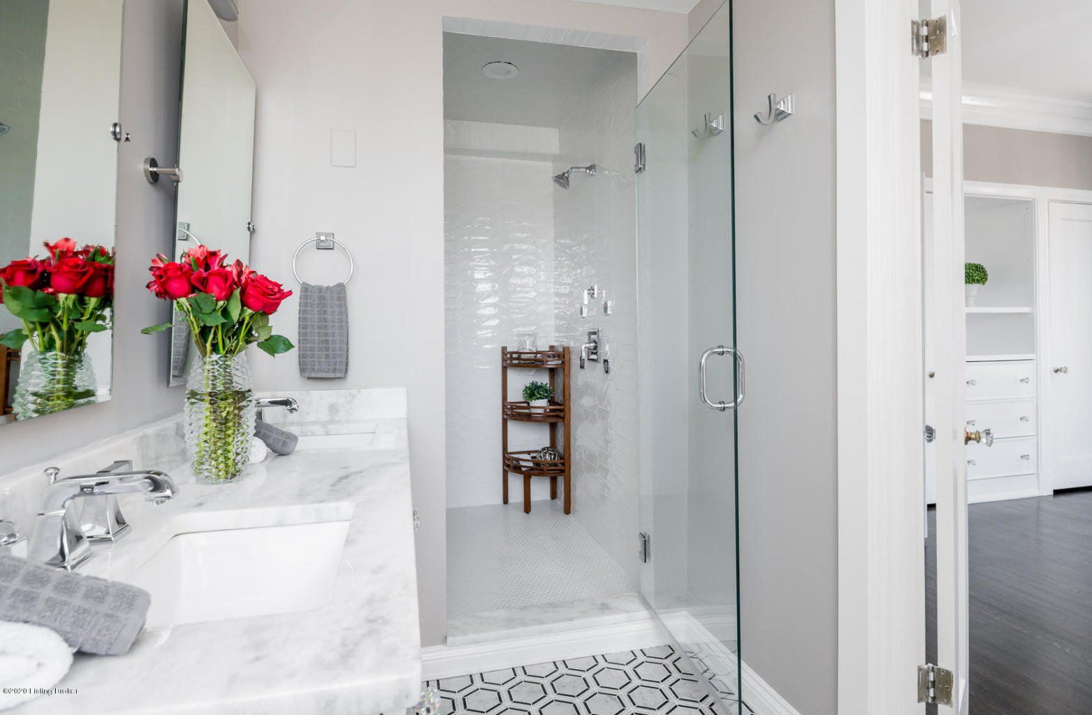 Elegant bathroom with marble countertop, glass shower, and red roses.