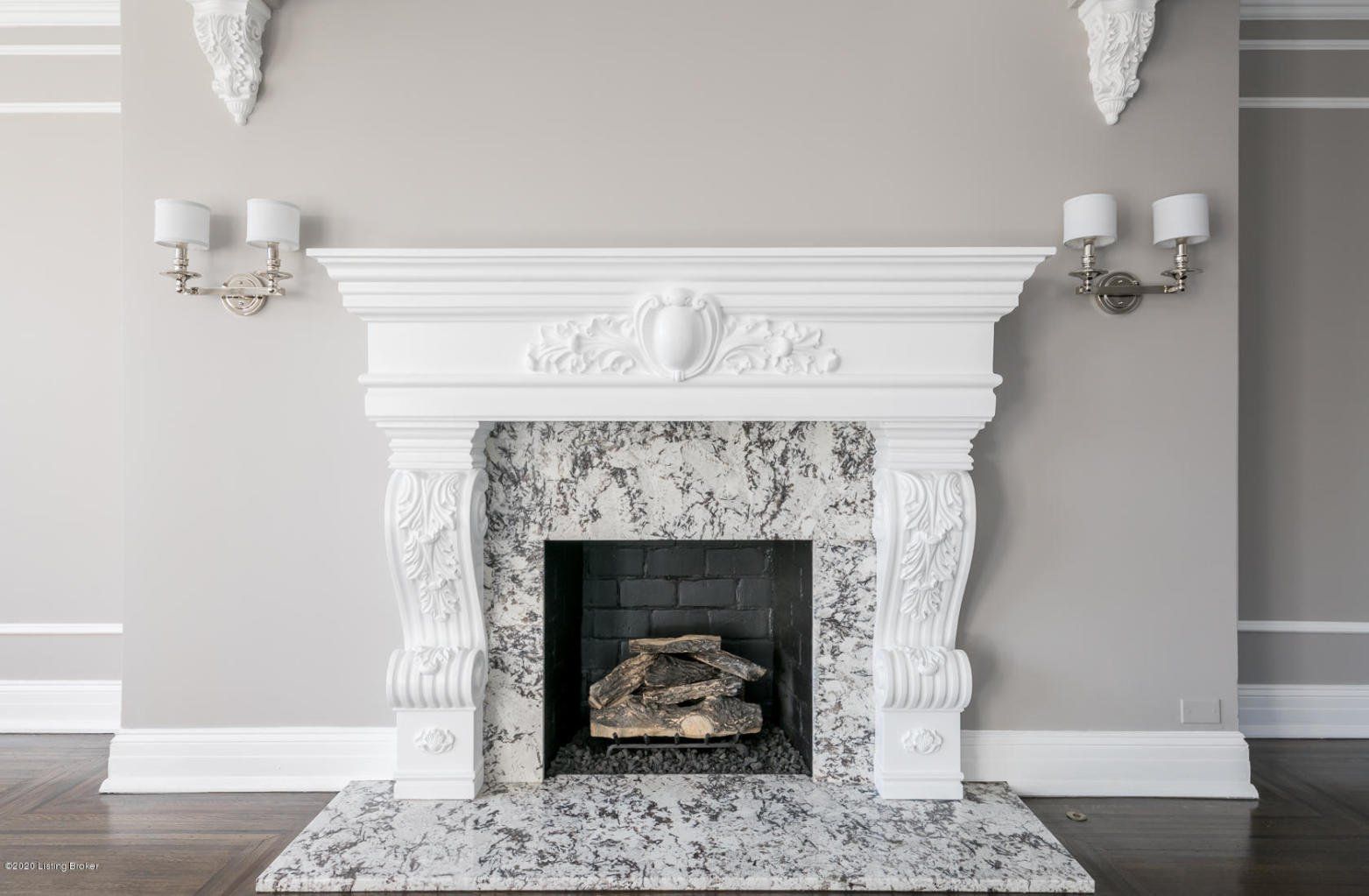 White marble fireplace with ornate carvings and gray speckled surround; gray wall.