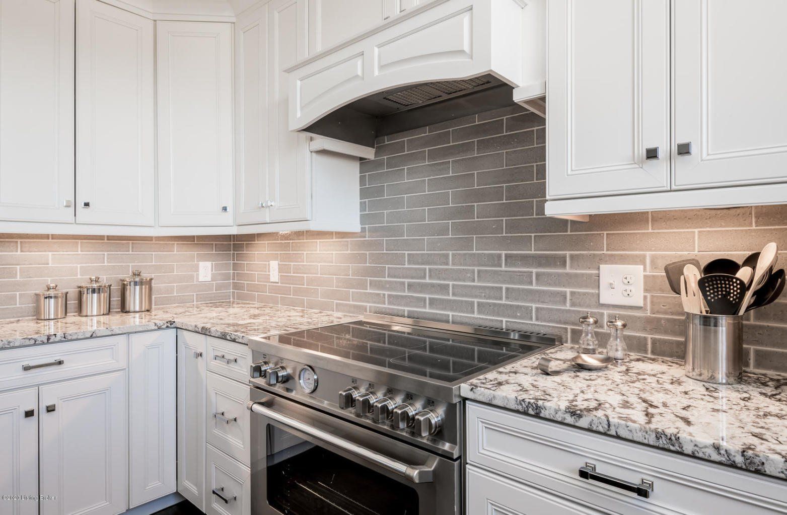 White kitchen with stainless steel oven, gray backsplash, and granite countertops.