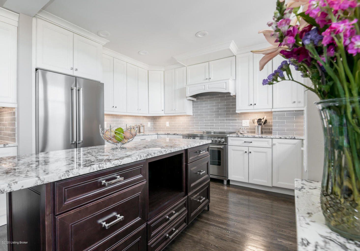 Modern kitchen with white cabinets, stainless steel appliances, dark island, and a vase of flowers.